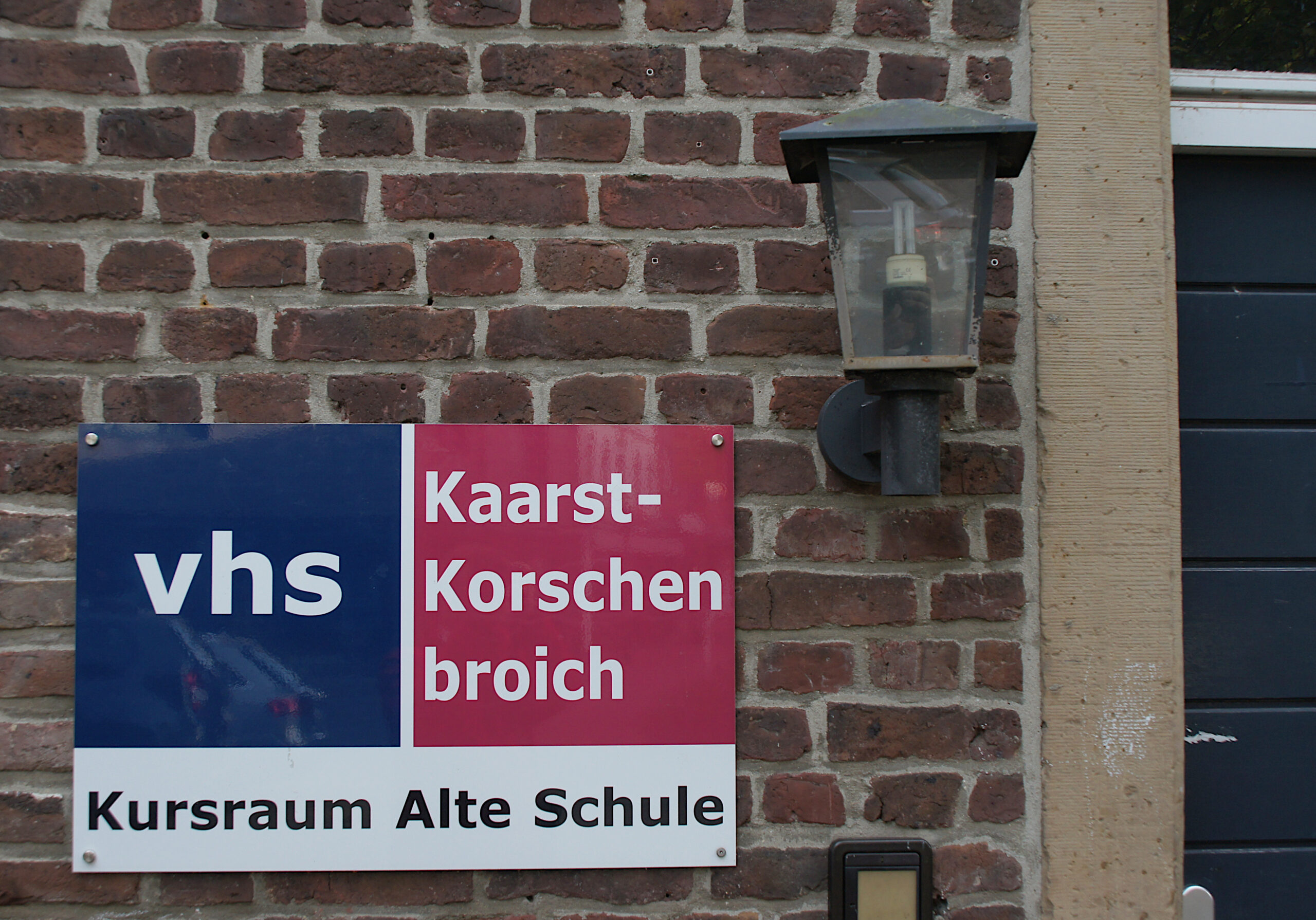 Schild der VHS Kaarst-Korschenbroich vor dem Eingang zum Kursraum an der Alten Schule.